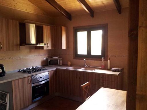 Cocina de madera con ventana, estufa y mesa. Ambiente acogedor y luminoso.