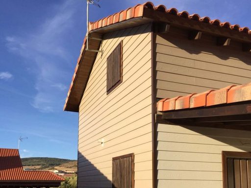 Casa prefabricada de dos plantas con tejado a dos aguas y ventanas cubiertas.