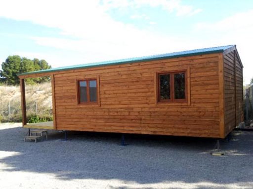 Casa de campo de madera con techo verde y ventanas, situada en un entorno natural.