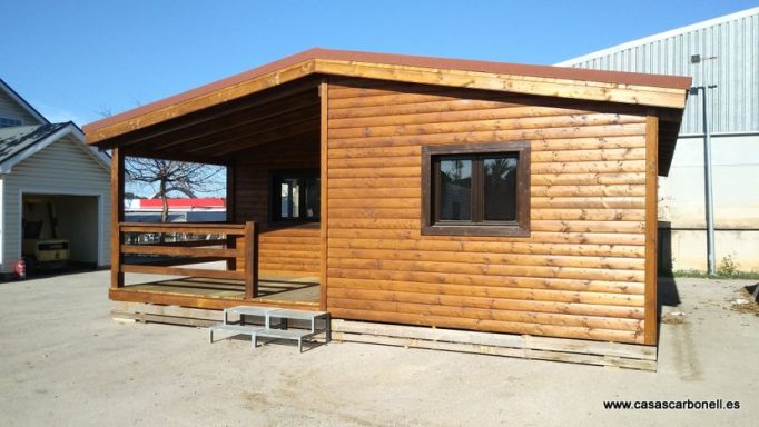 Casa prefabricada de madera con porche, ventanas oscuras y revestimiento de tablones.