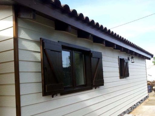 Casa prefabricada de madera con ventanas oscuras y contraventanas, paredes de color claro.