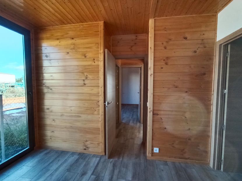 Interior de una habitación con paredes de madera y puerta abierta hacia otra habitación.
