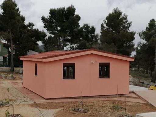 Casa prefabricada de color rosa con ventanas, situada en un entorno natural con árboles.