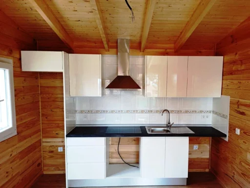 Cocina moderna con muebles blancos y encimera negra en un ambiente de madera.