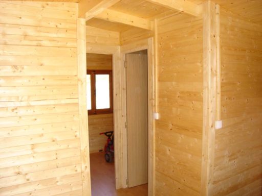 Interior de una cabaña de madera con paredes y puertas sin terminar.