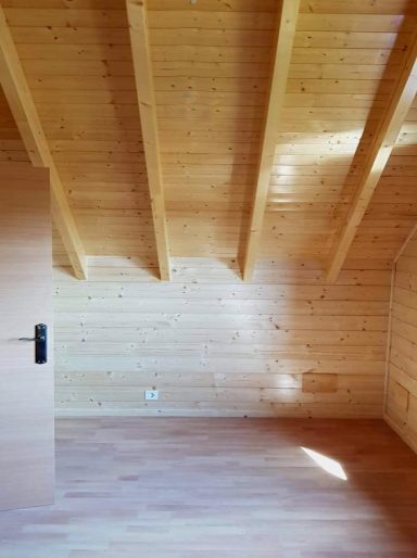 Interior de una habitación con paredes y techo de madera clara y suelos de madera.