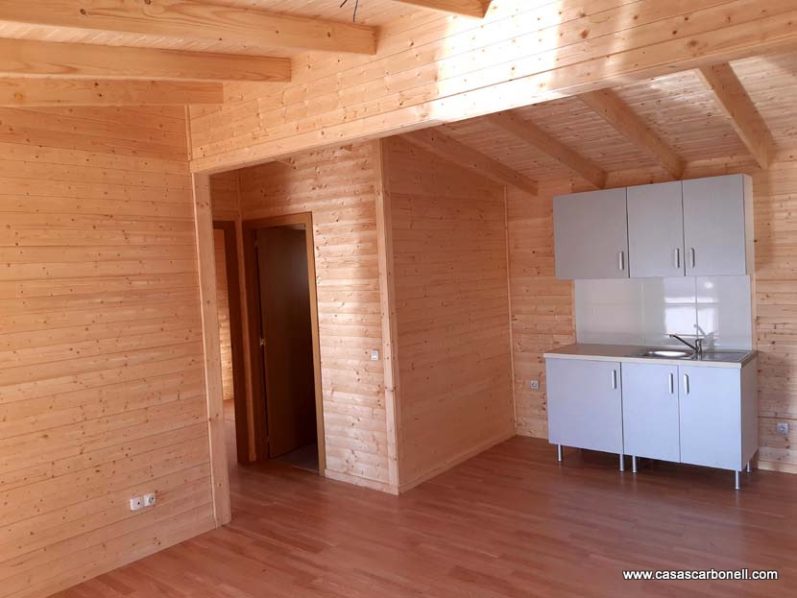 Interior de una casa de madera con cocina y paredes de paneles de madera clara.