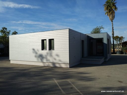 Casa prefabricada moderna de una sola planta, con paredes blancas y ventanales, en un entorno despejado.