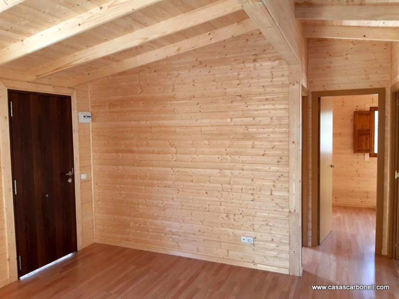 Interior de una habitación de casa de madera con paredes claras y suelo laminado.