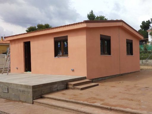 Casa prefabricada Madrid de una planta con paredes de color peach y ventanas oscuras, ubicada en un terreno.