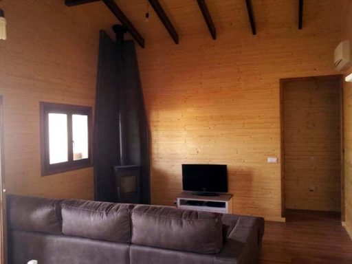 Interior de una sala con sofá, televisor y chimenea de leña en una casa de madera.