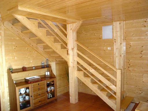 Escalera de madera clara en una habitación con paredes y suelo de madera. Mueble en la esquina.