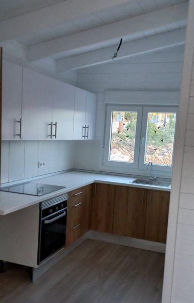 Cocina moderna con armarios blancos y de madera, equipada con horno y ventana amplia.